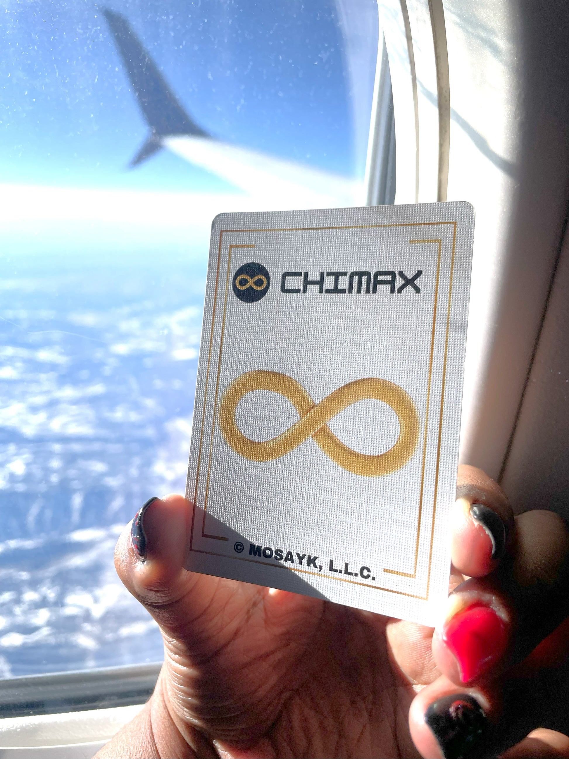 Card with Chimax logo held in front of a window with a view of clouds and a building.